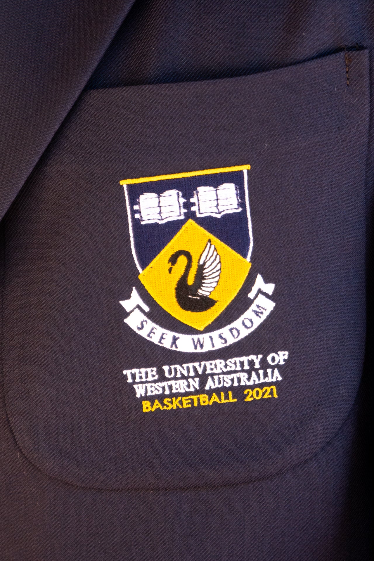 An extreme close up of the breast pocket of the UWA Blues Blazer. The pocket is embroided with the UWA crest.